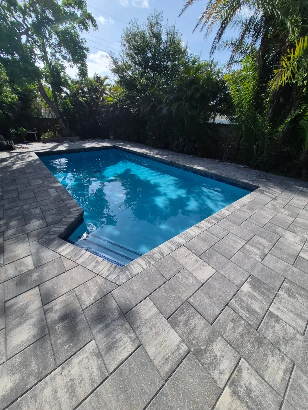 After: large-format paver deck, new coping and dark waterline tile on a Fort Myers job