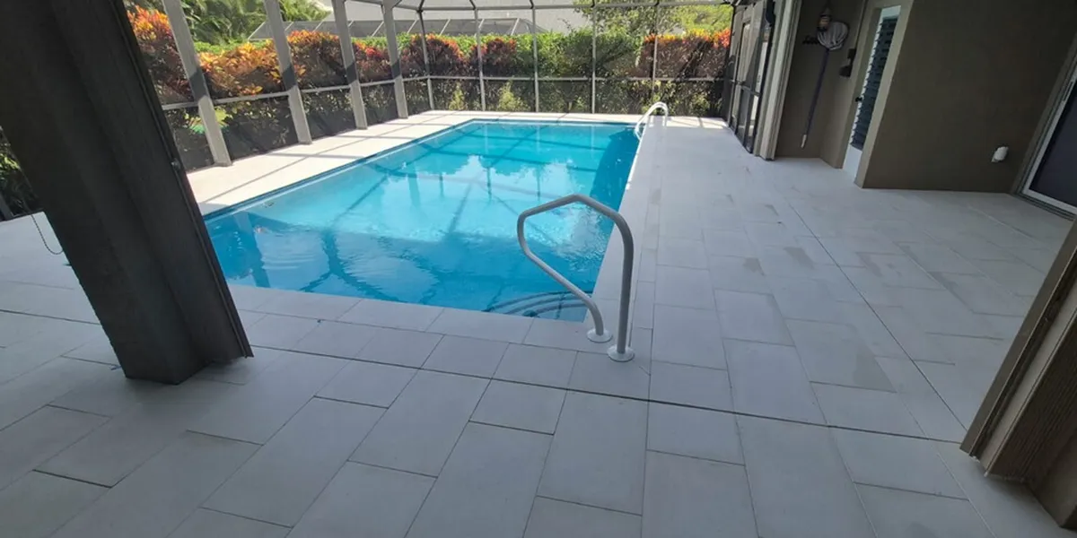 After: the same screened pool with the old pavers replaced by large light gray terrazzo pavers across the deck, the pool edge and the covered lanai
