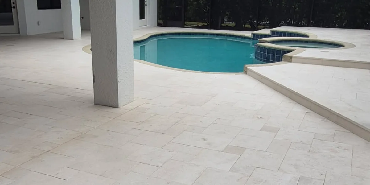 After: the same pool and spa with the old pavers replaced by a shellstone travertine deck laid in a French pattern across the lanai and the raised spa deck, under a screened enclosure